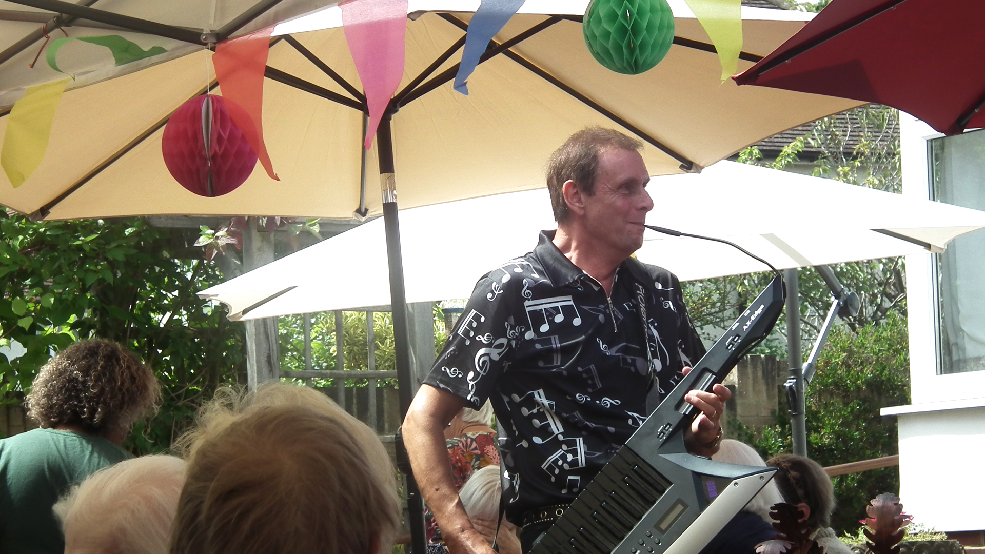 An entertainer at the summer party smiles while playing a melodica instrument and walking around the residents and visitors