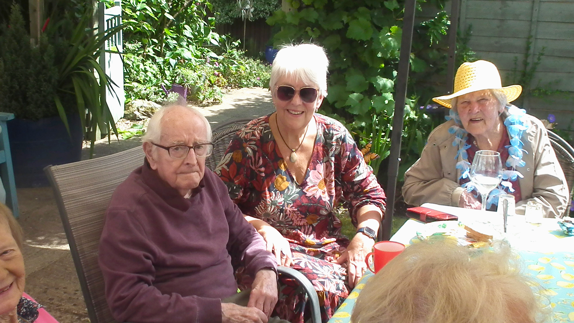 A care home resident sits outside under an umbrella with his family members at the summer party