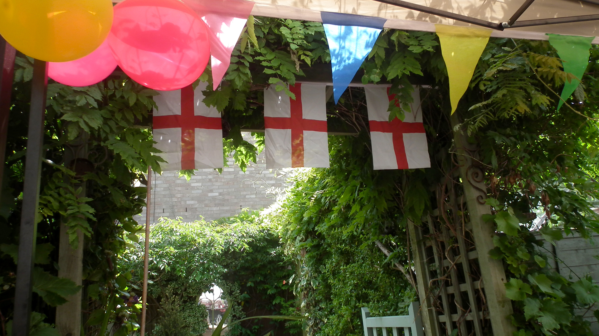 Decorations from the care home summer party, colourful bunting and balloons and England flags hang above the garden archway