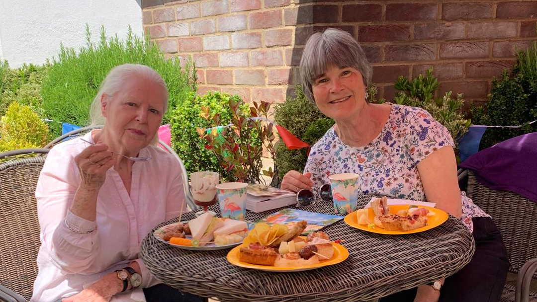 Care home resident sat with family at the summer party eating party food.