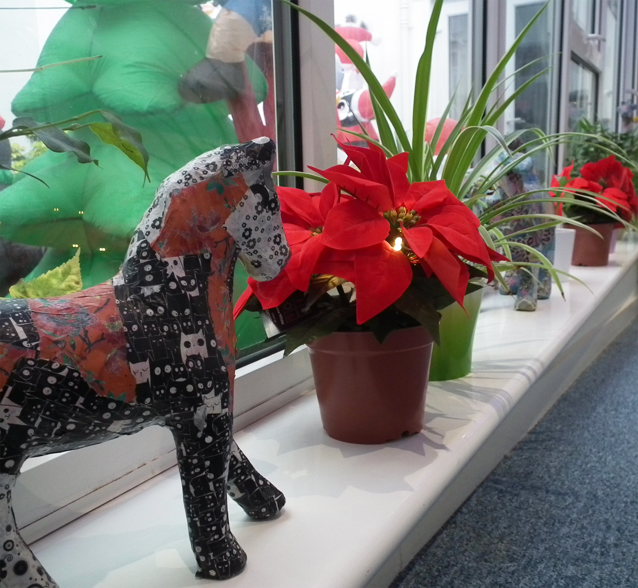 Vibrant red poinsettia flowers line up along the corridor next to paper-mache horses