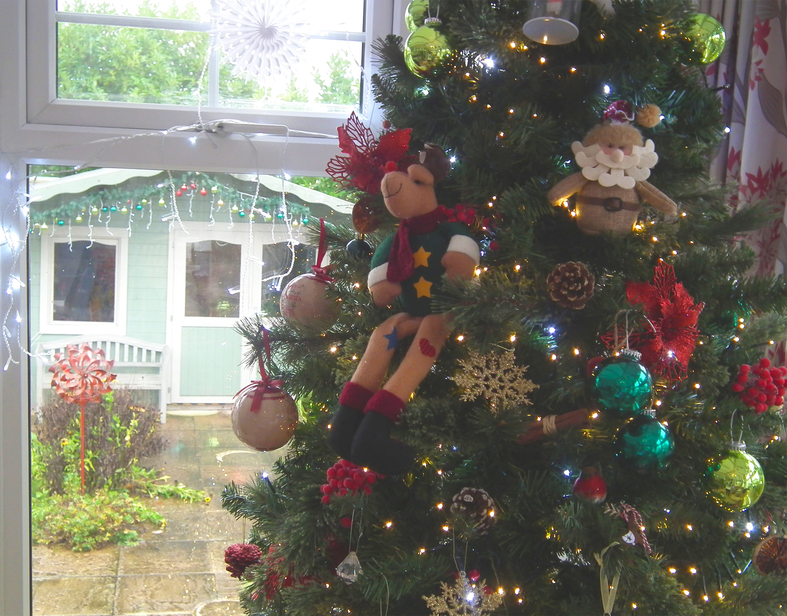 Close-up photo of one of the Christmas trees, featuring decorations of reindeer, Father Christmas, robins, baubles and lights. Outside in the background the shed can be seen decorated with garland and baubles