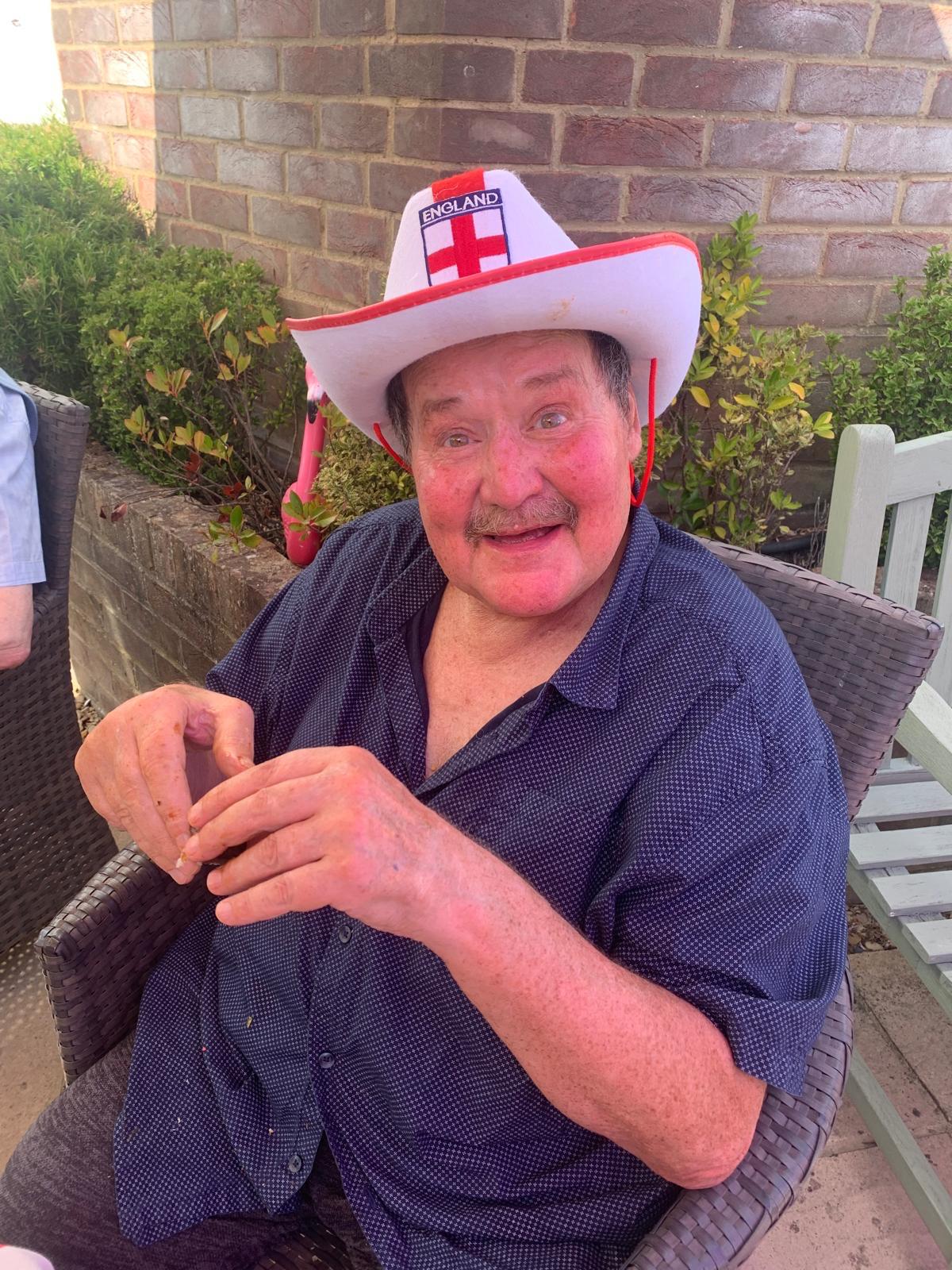 A resident smiles and wears an English flag cowboy-hat while sitting in the garden