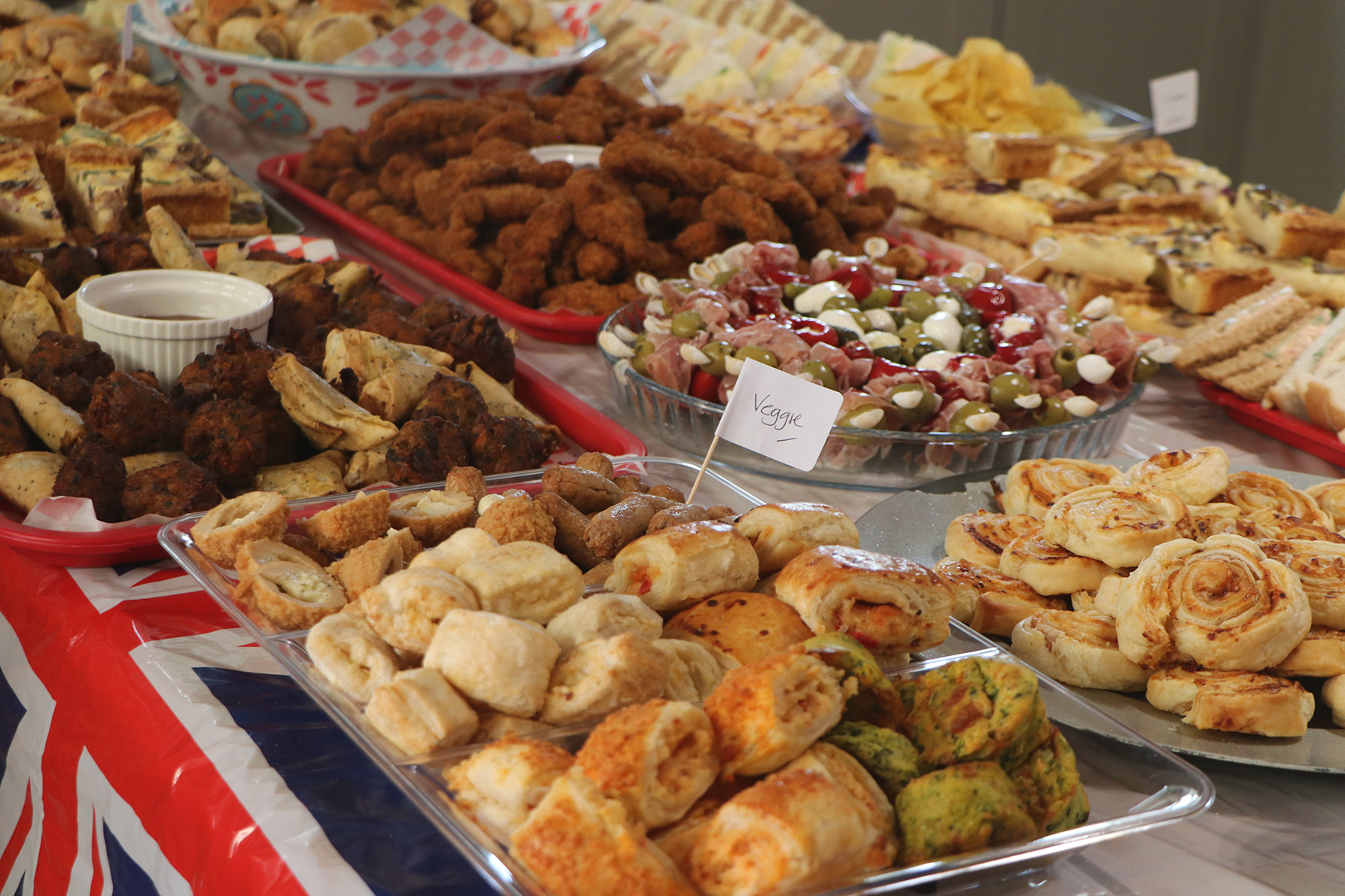 Buffet of food with a close-up of a veggie platter including sausage rolls, pastries and scotch eggs