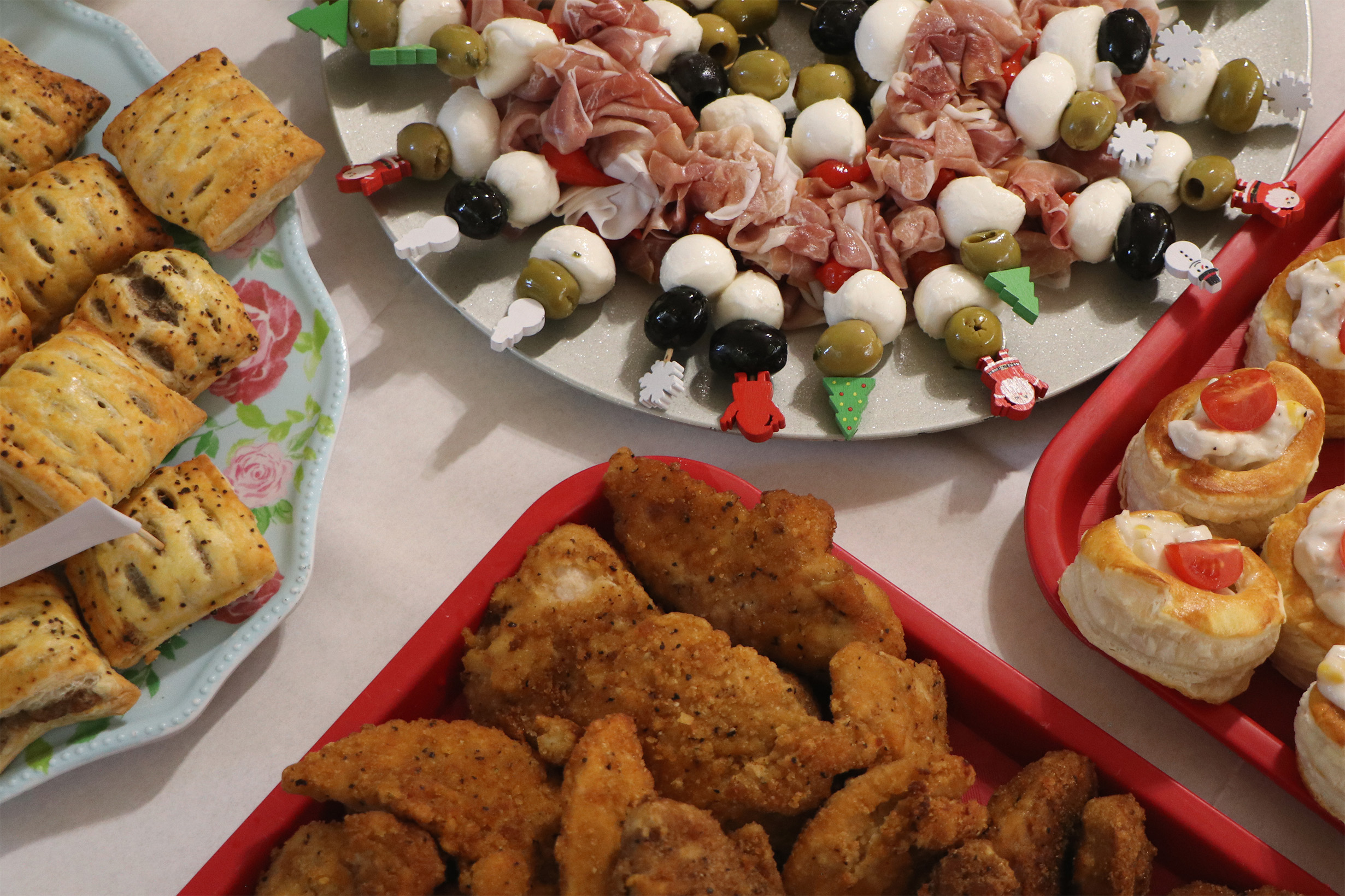 A closeup photo of the Christmas party food including mini sausage rolls, mozzarella balls, olives, prosciutto and more.