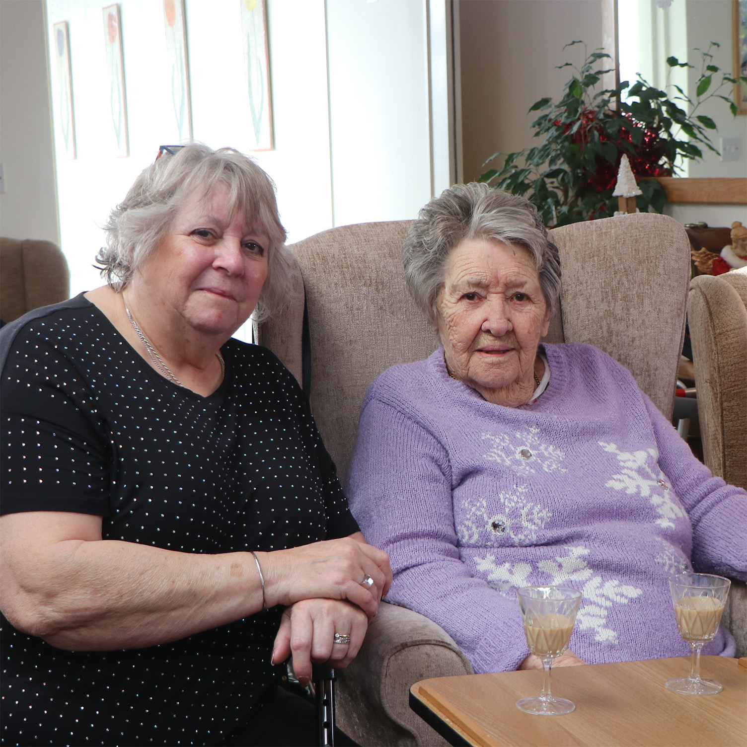 Resident and family member sit with a festive drink and a purple snowflake jumper.