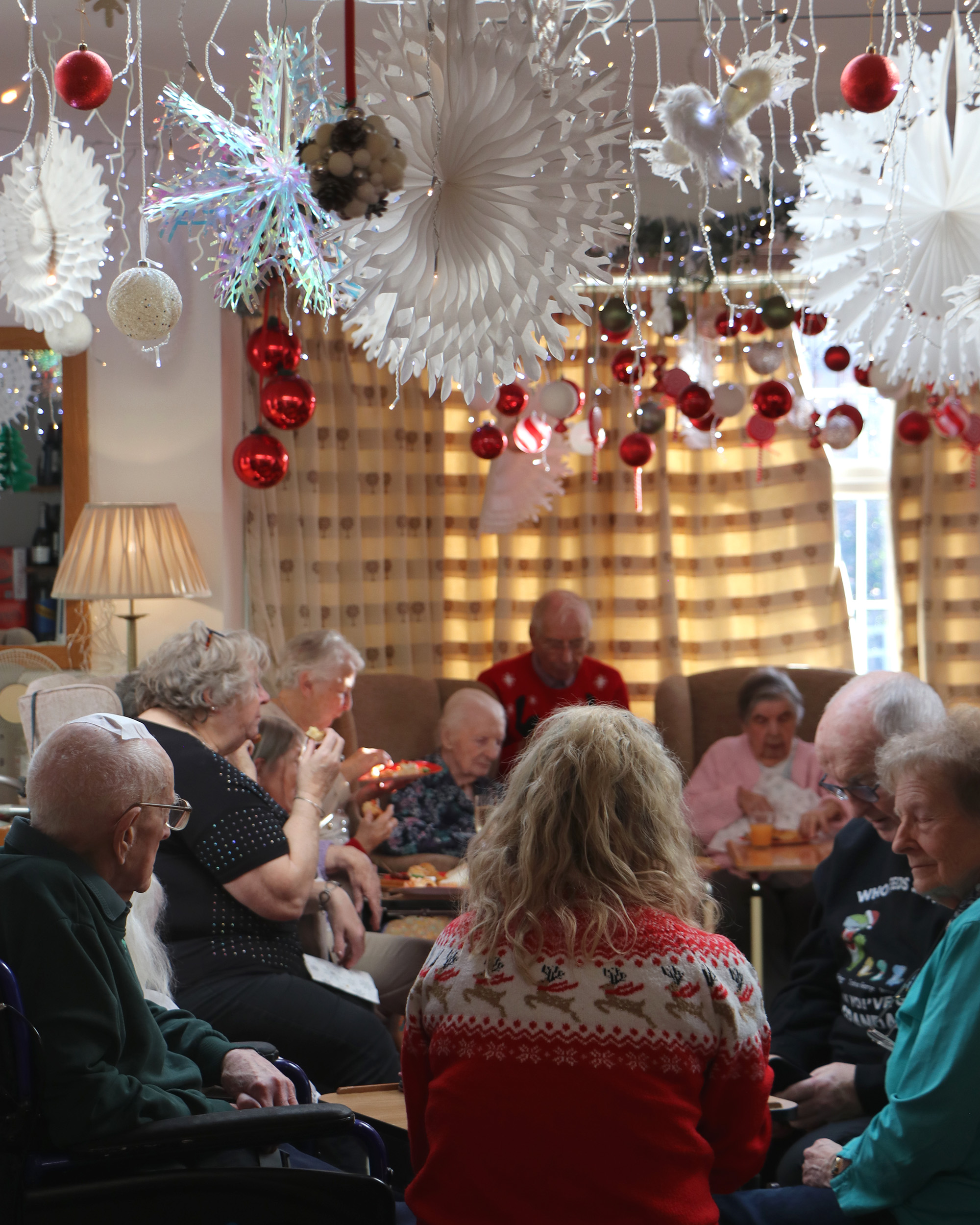 Residents and family members sit and chat at the Christmas party, wearing Christmas jumpers and surrounded by Christmas decorations.
